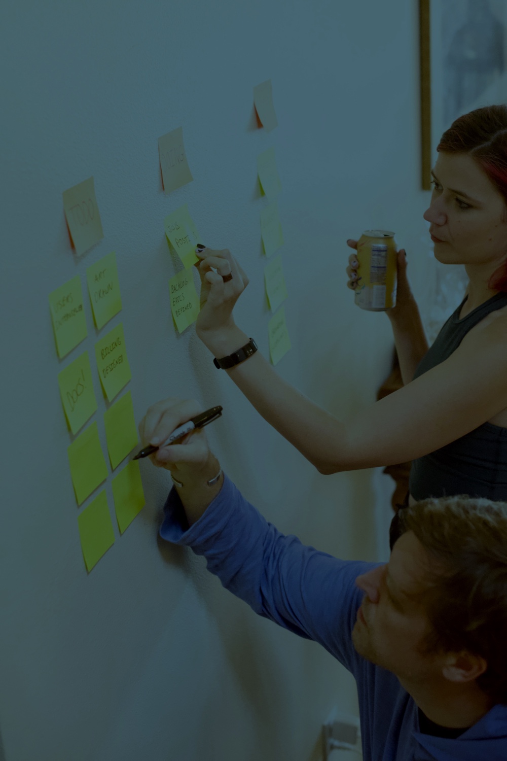 Two people writing on sticky notes on a wall.