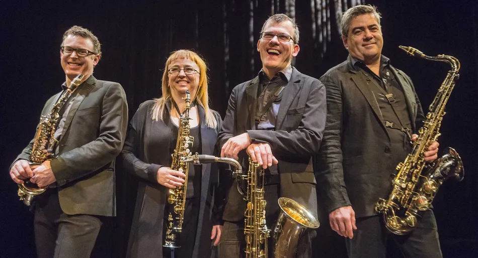 Quatre musiciens souriants avec des saxophones sur scène.